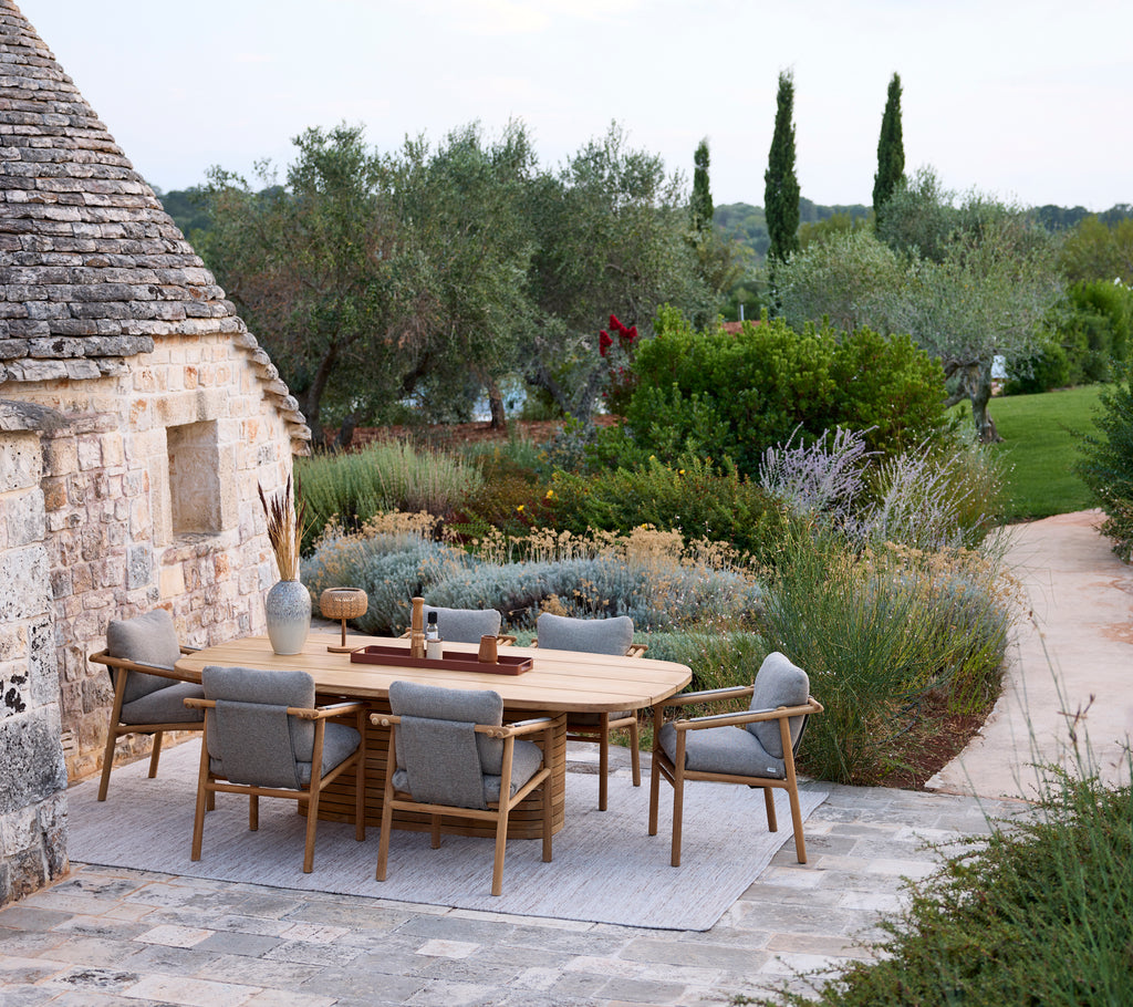 Modern outdoor dining setup with a round table and grey chairs surrounded by greenery.