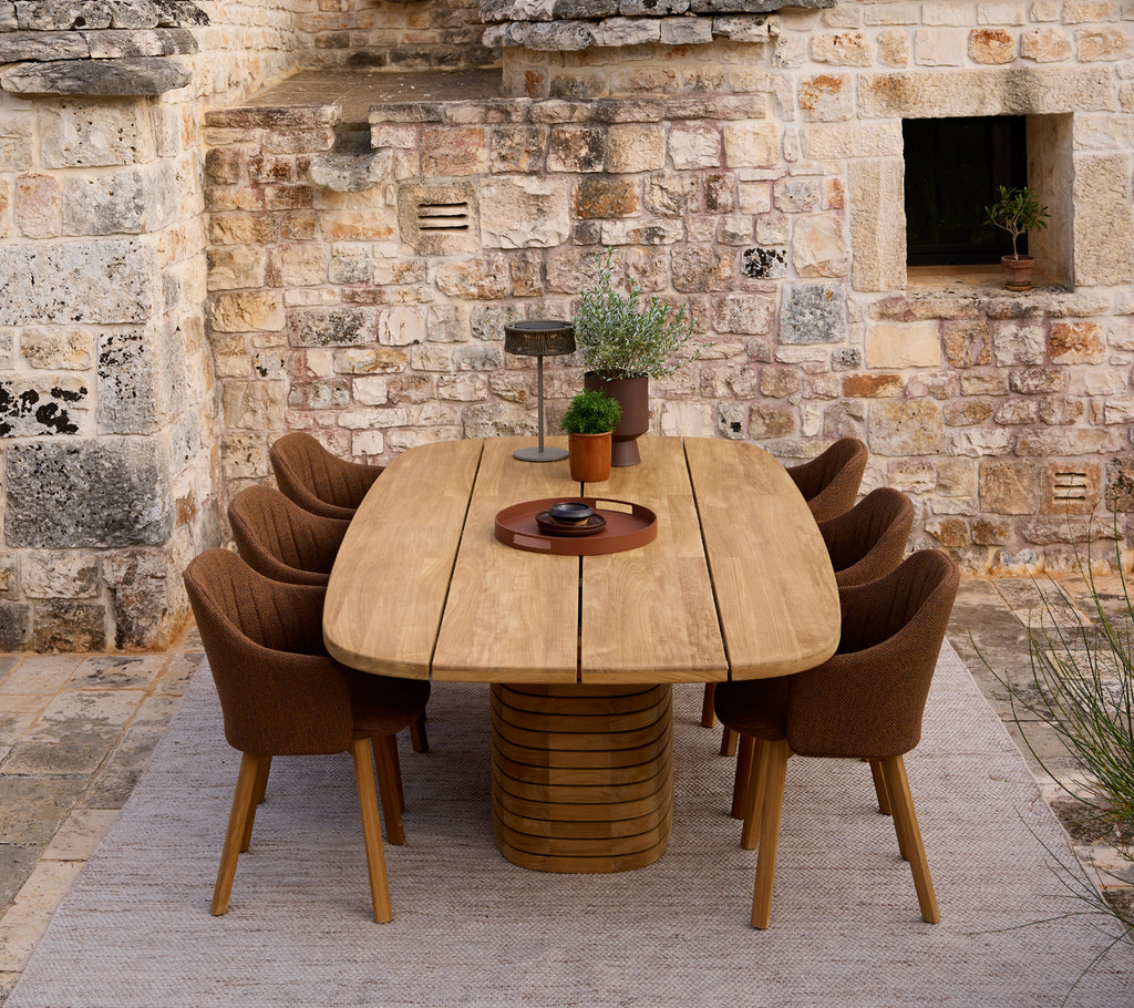 Modern wooden dining table surrounded by brown chairs in a rustic setting.