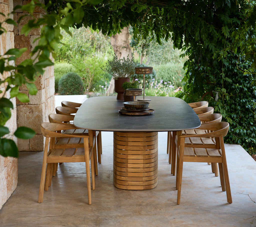 Modern outdoor dining table with wooden chairs surrounded by greenery.