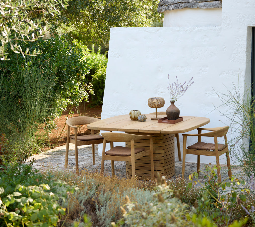 Modern round table with wooden chairs and decorative vase in an outdoor setting.