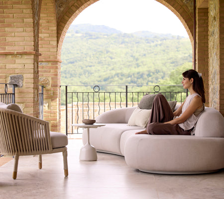 A serene seating area featuring a mellow lounge sofa, a Moments lounge chair, and a Glaze coffee table, with lush greenery in the background.