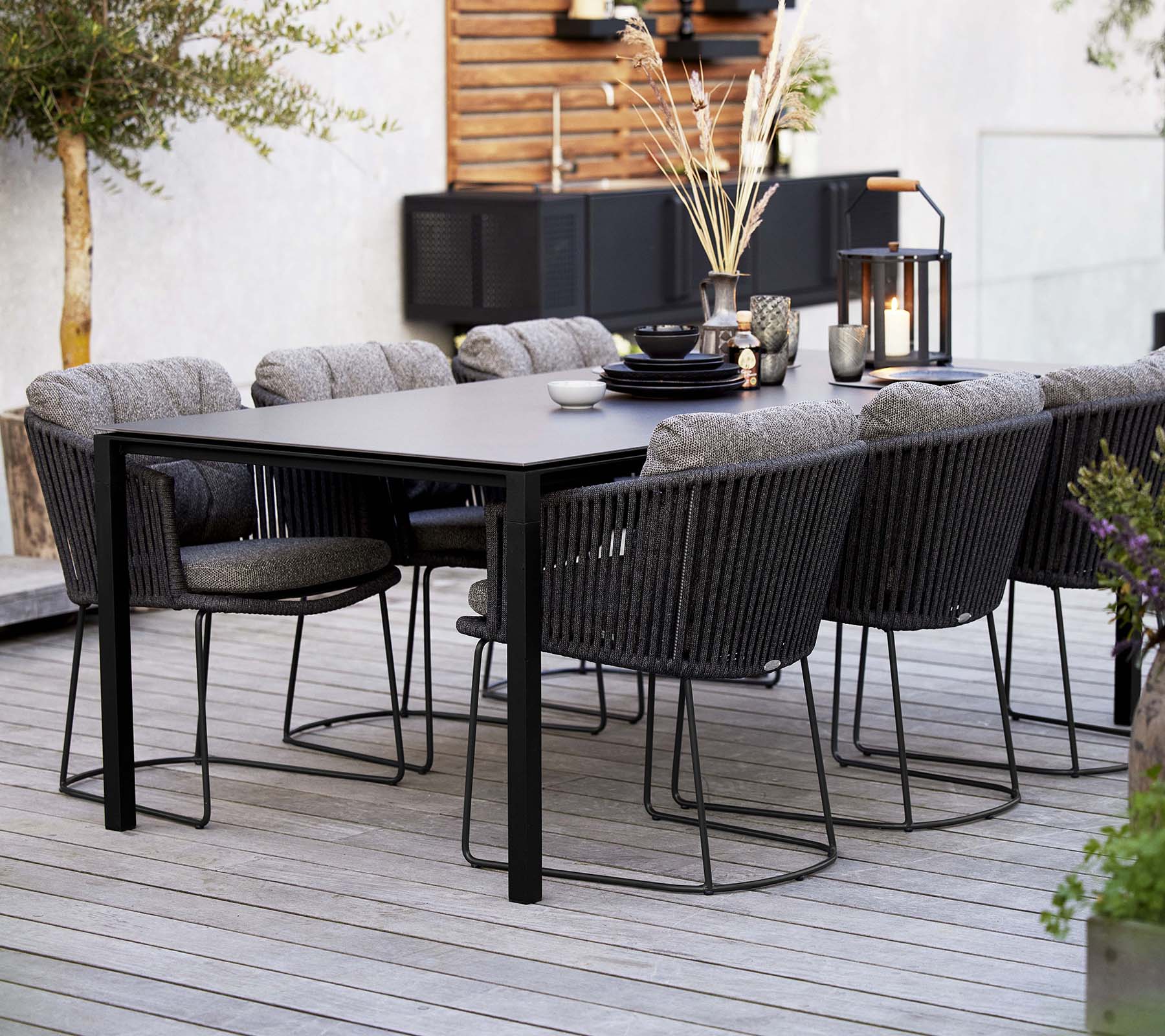 A stylish dining setup featuring a sleek table surrounded by comfortable woven chairs, adorned with decorative elements and plants.
