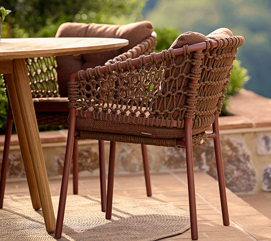 A stylish red chair with woven details next to a wooden dining table, complementing a relaxed outdoor setting.