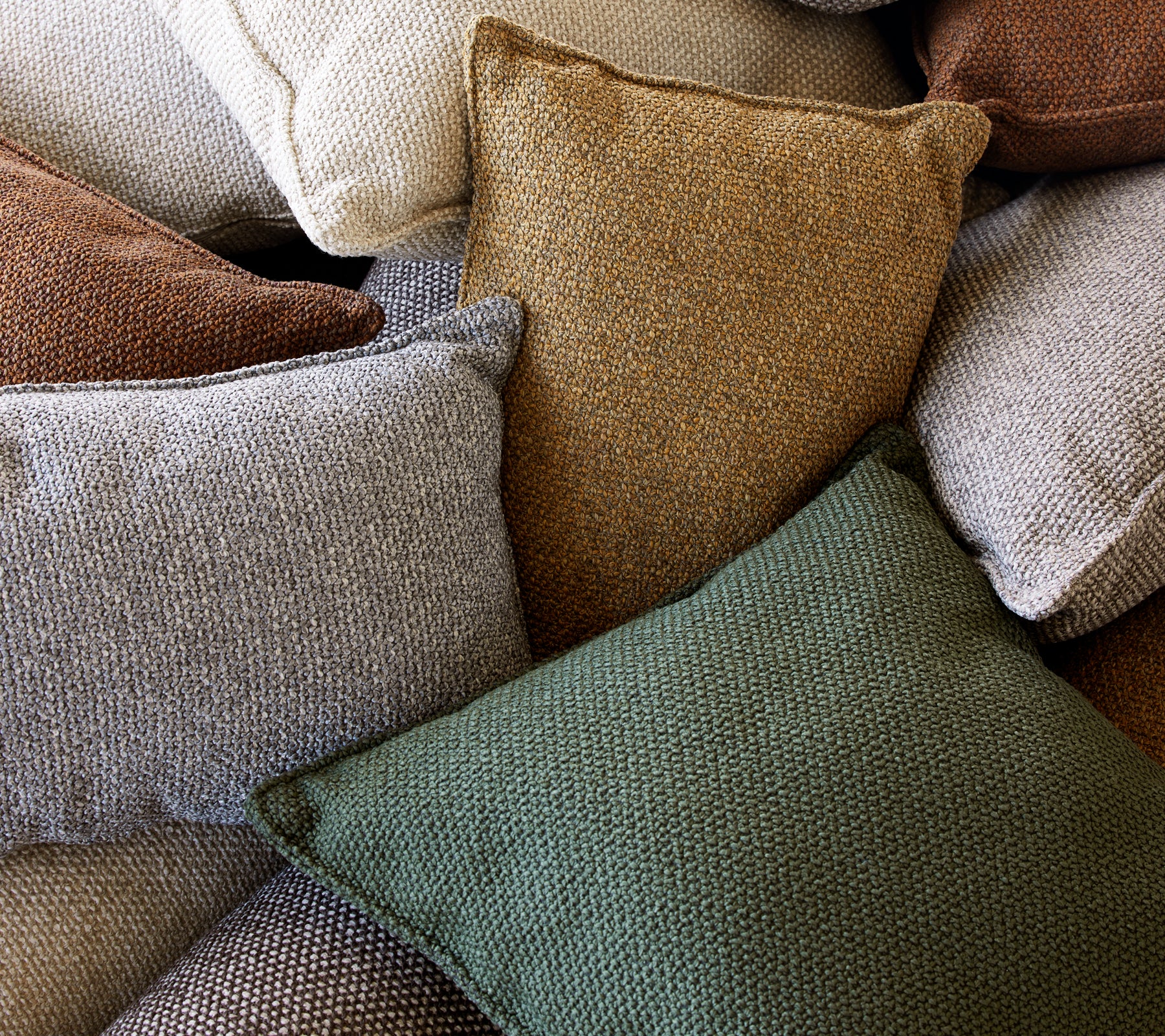 A collection of textured scatter cushions in various colors, including green, brown, and cream, stacked together.