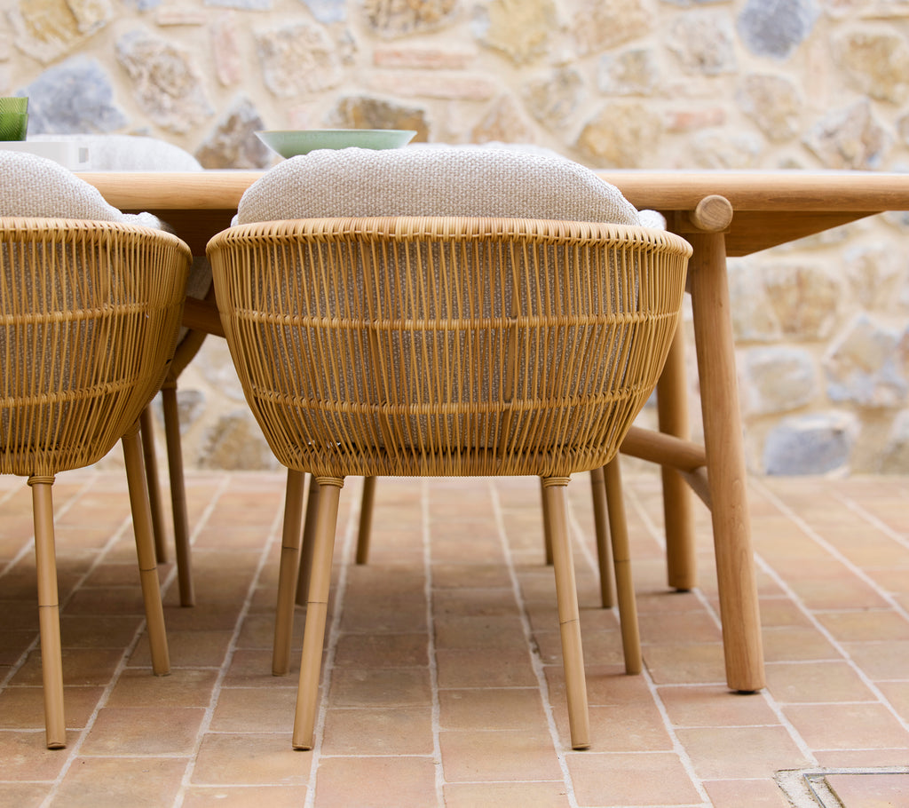 Two woven dining chairs with aluminium legs positioned beside a wooden dining table, featuring a natural aesthetic.