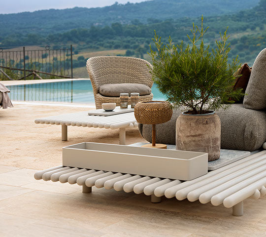 Stylish outdoor seating with aluminum sticks, a round plant pot, and decorative elements, set against a serene landscape.