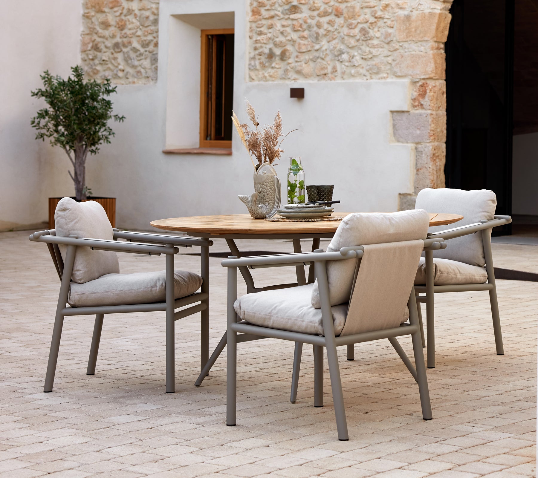 Modern dining table with a wooden top and aluminum frames, accompanied by soft, cushioned chairs, set against a textured background.
