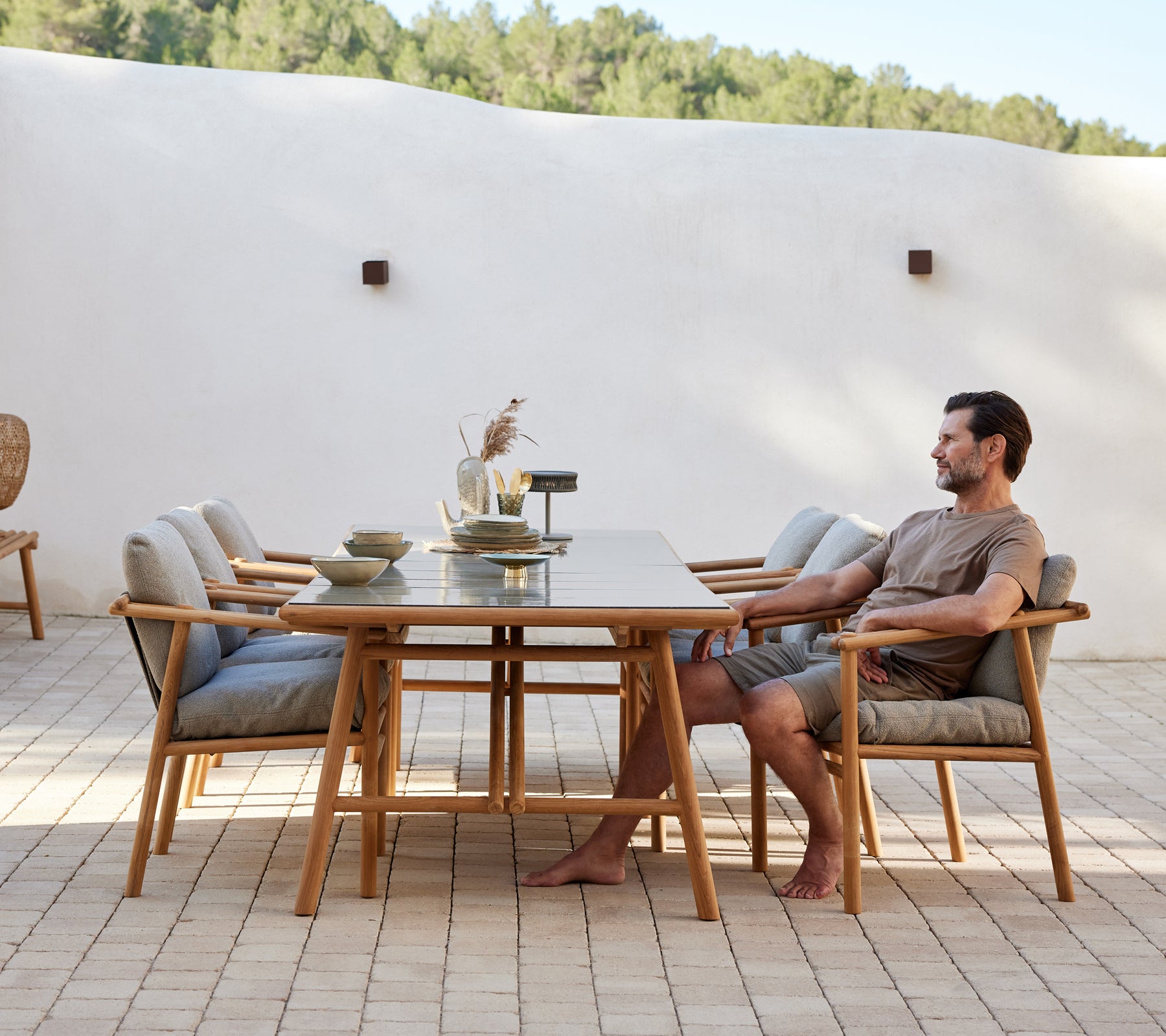 A teak dining setup featuring a long table and comfortable chairs, with a person seated, creating a relaxed dining atmosphere.
