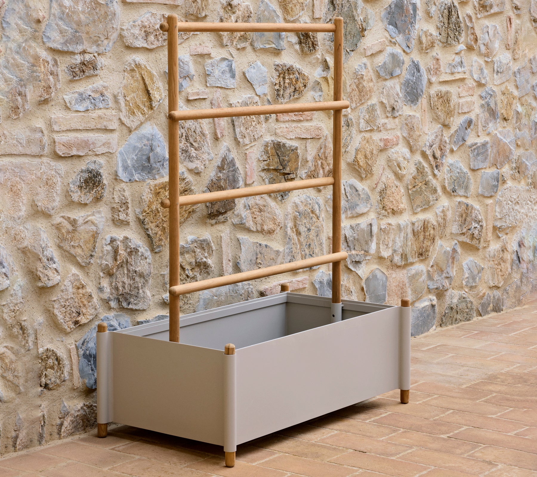 A grey aluminium planter with a wooden ladder support, designed for growing plants, set against a textured stone wall.