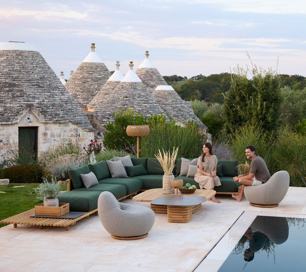 Modern outdoor lounge area with green sectional sofa and grey chairs by a pool.