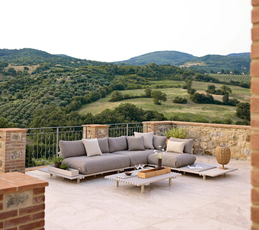 Stylish lounge area featuring a grey sectional sofa and a wooden coffee table, surrounded by lush hills and a scenic landscape.
