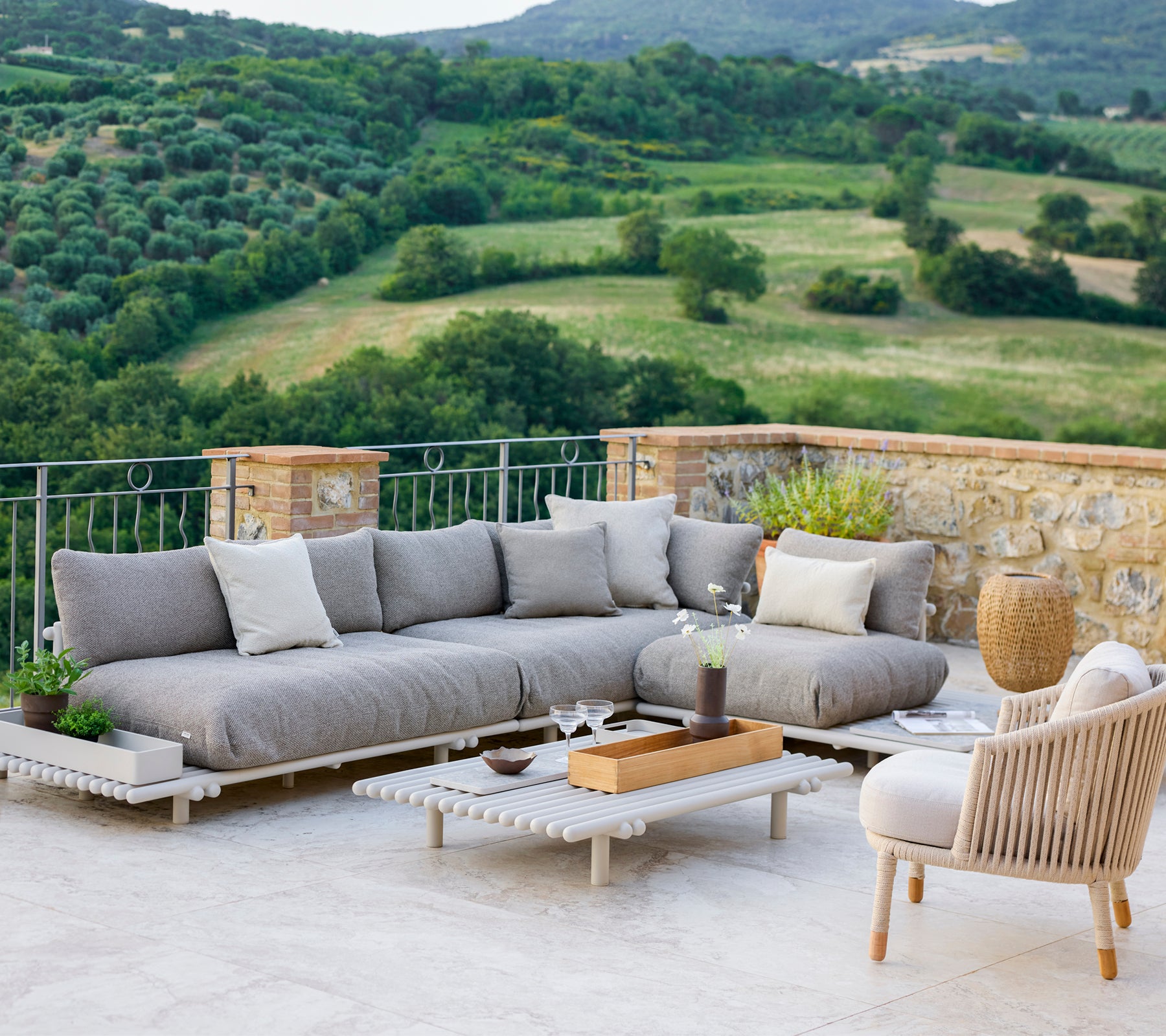 Stylish lounge area featuring a grey sectional sofa and a comfortable chair, set against a scenic landscape.