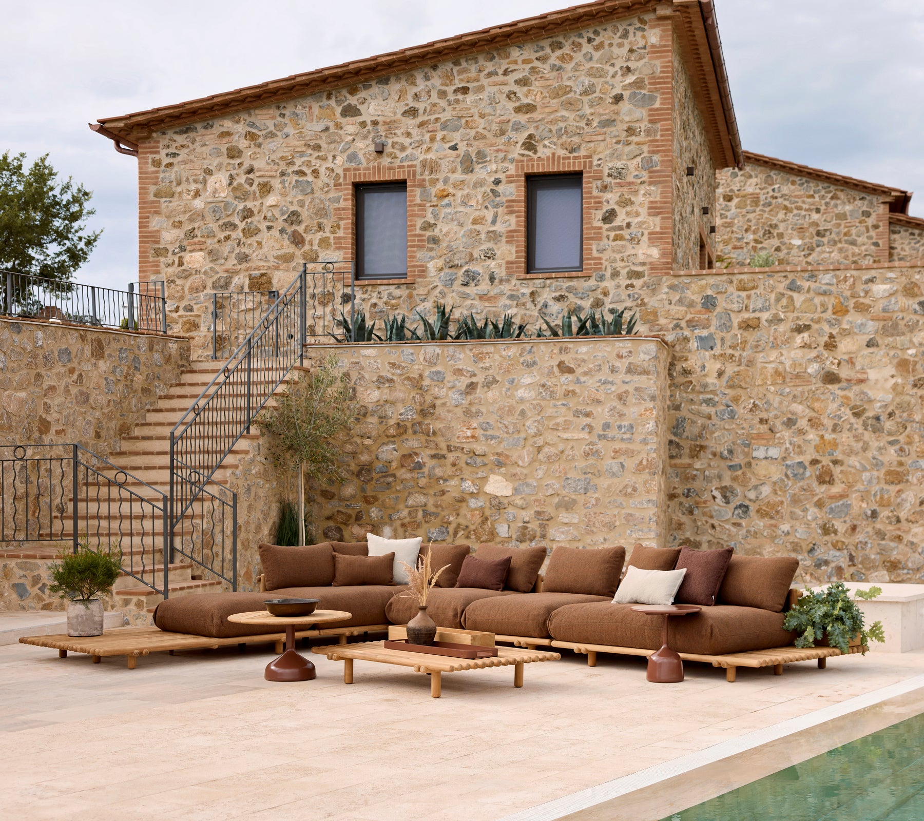 Lounge sofa with plush cushions alongside a stylish coffee table, set against a stone wall backdrop. Planters add a natural touch.