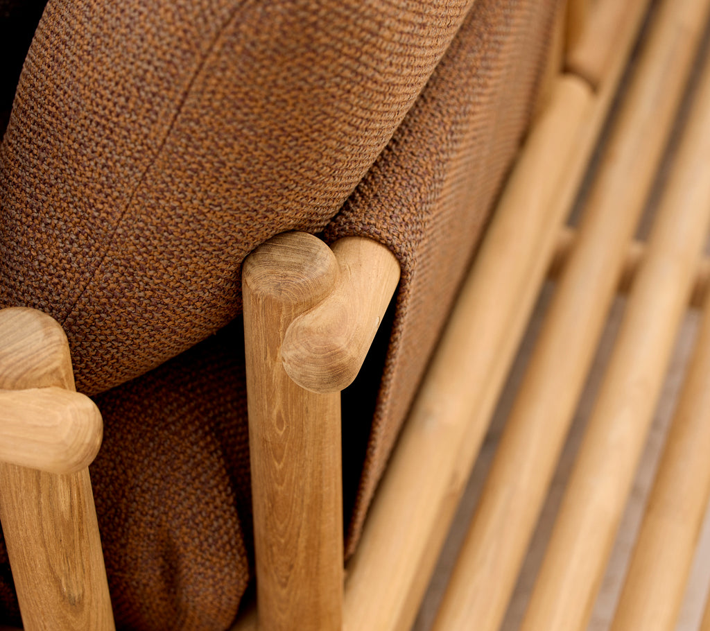 Teak lounge chair featuring soft cushions and stylish wooden sticks forming the armrest and base structure.