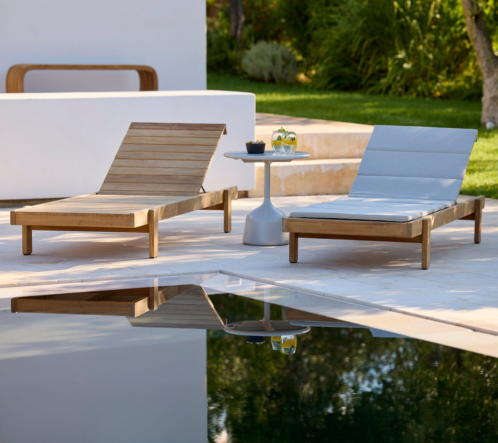 Modern wooden lounge chairs with grey cushions beside a small round table in an outdoor setting.