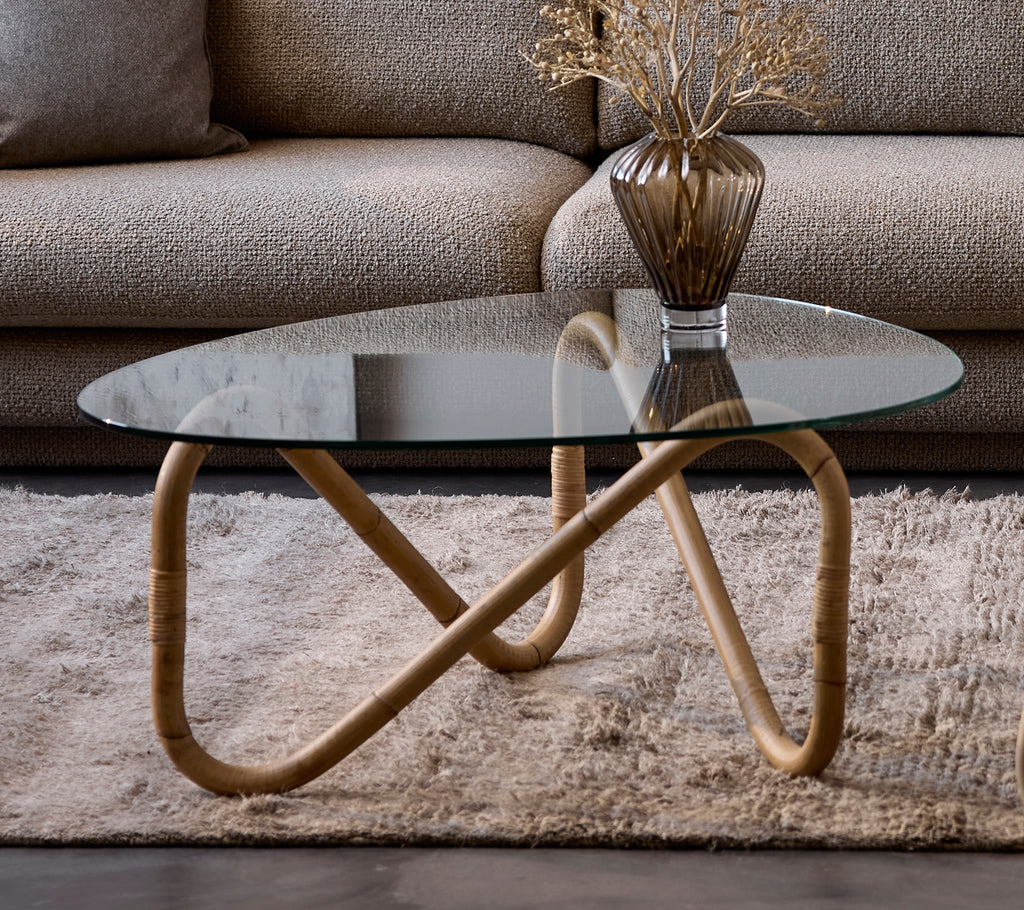 Modern glass coffee table with a beige vase on a rug in a lounge setting.