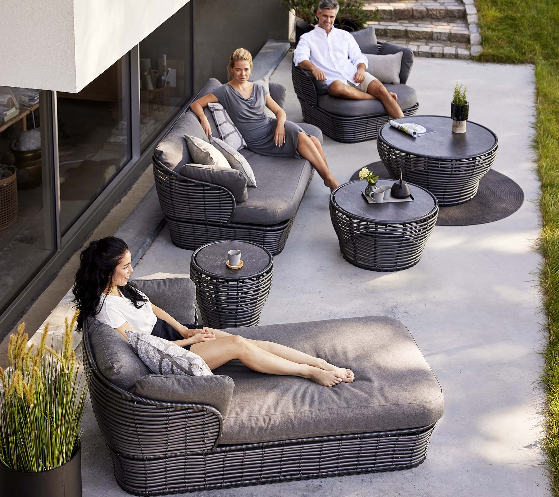 Contemporary lounge area featuring a basket daybed, a 3-seater sofa, and lounge chairs, complemented by circular tables and decorative plants.